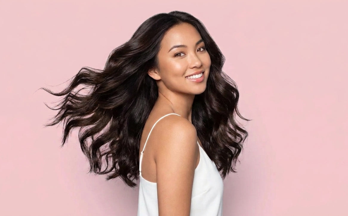 Woman with long, wavy hair smiling against a pink background